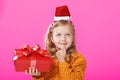 Portrait of a little girl in a sweater and a santa claus hat on a pink background.