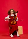 Portrait of little girl, talanted musician wearing huge mother& x27;s sundress playing violin, having fun isolated over