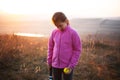 Portrait of little girl is training skill, outside of tennis court, in field at sunset. Wearing pink sweater.