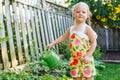 Little girl watering green plants on backyard