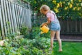 Little girl watering green plants on backyard