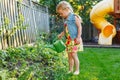 Little girl watering green plants on backyard