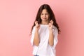 Little girl crossing fingers in hope for good luck, making wish, rituals, standing with closed eyes. Royalty Free Stock Photo