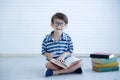 Portrait of little happy Caucasian boy wear glasses sitting on the floor looking at camera and reading a big book at home. Royalty Free Stock Photo