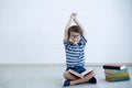 Portrait of little happy Caucasian boy wear glasses sitting on the floor looking at camera and reading a big book at home. Royalty Free Stock Photo