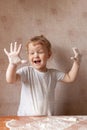 portrait little happy girl standing wooden table flour, laughing, raising her hands soiled flour. concept childhood. Royalty Free Stock Photo