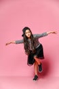 Portrait of a little hipster girl in a dark dress with a baseball cap and sneakers, on a pink background Royalty Free Stock Photo