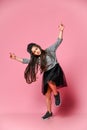 Portrait of a little hipster girl in a dark dress with a baseball cap and sneakers, on a pink background Royalty Free Stock Photo