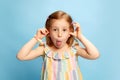 Portrait of little joyful, pretty girl child playing, posing with funny grimacing face against blue studio background Royalty Free Stock Photo