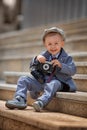 Portrait of a little kid boy photographer taking picture with retro vintage photo camera on the steps outside Royalty Free Stock Photo