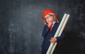 Portrait of little kid in safety helmet and suit thinking about aspirations. Little businessman in glasses looking up