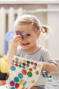 Portrait of a little lovely girl. Cute toddler sticks stickers on herself. Lovely blonde baby in a blue t-shirt.