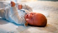 Portrait of little newborn baby sucking soother or pacifier and starting to cry in crib at night. COncept of crying Royalty Free Stock Photo