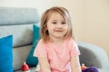 Portrait of a little pretty girl in a pink t-shirt, sitting in her room on the couch, looking at the camera, close-up Royalty Free Stock Photo