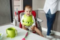 Portrait of little scared baby boy sitting in baby chair in kitchen, crying and screaming while mother cooking him food. Royalty Free Stock Photo