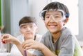 Portrait of little scientist Asian boy in safety glasses smiling at the camera while examining a test tube in science class. Royalty Free Stock Photo