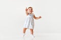 Portrait of little smiling baby girl, toddler in beautiful dress walking and raising finger in curiosity against white Royalty Free Stock Photo