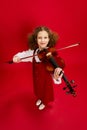 Portrait of little girl, talanted musician wearing huge mother& x27;s sundress playing violin, having fun isolated over