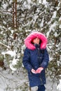 Portrait of little smiling happy girl in pink warm fur hood walking outside on nature winter snowy forest background Royalty Free Stock Photo