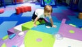 Portrait of little toddler boy crawling and playing on the colorful children palyground covered with soft mats in