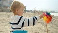 Portrait of little toddler boy playing with spinning colorful pinwheel toy on the sandy sea beach. Concept of summer holiday, Royalty Free Stock Photo