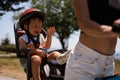 Portrait of little toddler boy with security helmet on the head sitting in bike seat and his mother with bicycle. Safe