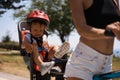 Portrait of little toddler boy with security helmet on the head sitting in bike seat and his mother with bicycle. Safe