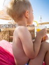 Portrait of little toddler boy sitting on hte sun bed at sea beach and drinking orange juice from straw Royalty Free Stock Photo