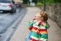 Portrait of little toddler girl on rainy day. Happy positive child running through rain, puddles. Preschool kid with