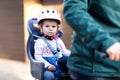 Portrait of little toddler girl with security helmet on the head sitting in bike seat and her father or mother with