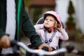 Portrait of little toddler girl with security helmet on the head sitting in bike seat and her father or mother with