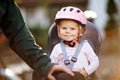 Portrait of little toddler girl with security helmet on the head sitting in bike seat and her father or mother with