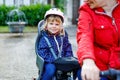 Portrait of little toddler girl with security helmet on the head sitting in bike seat and her mother with bicycle. Safe