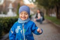 Portrait of a little toddler with a happy tricky face walking along the spring park alley. While His father squatted down in the