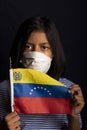 Portrait of little girl wearing medical mask and holding hopefully the flag of Venezuela