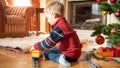 Portrait of little 3 years old boy sitting next to Christmas tree and playing with toy railroad. Child receiving Royalty Free Stock Photo