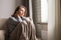 Portrait of lonely sad ÃÂaucasian young woman wrapped in a plaid sitting near window of apartments. Royalty Free Stock Photo