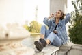 Portrait of a longing smiling teenage girl dressed in denim and boots, sitting outside Royalty Free Stock Photo