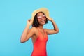 Portrait of lovely black lady in straw hat and swimsuit posing and smiling at camera on blue background Royalty Free Stock Photo