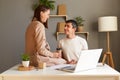 Portrait of lovely couple posing in office together, man sitting at desk and looking at her wife who sitting on table, male and Royalty Free Stock Photo