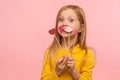 Portrait of lovely cute surprised little girl looking with amazement, holding few red pink paper lips on sticks