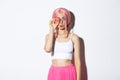 Portrait of lovely girl in pink wig, dressed up for party or holiday celebration, holding delicious macaroon and pouting