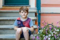 Portrait of lovely gorgeos school kid boy sitting infront of house. Happy healthy boy on stairs by home.