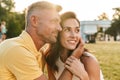 Portrait of lovely middle-aged couple looking aside at copyspace and hugging while sitting on grass in summer park Royalty Free Stock Photo