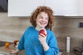 Portrait of a lovely smiling pretty girl biting an apple in her kitchen. Young woman enjoying her red organic apple fruit. Daily Royalty Free Stock Photo