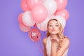 Portrait of lovely sweet chick having many air balloons blowing kiss with pout lips palm to the camera isolated on pink