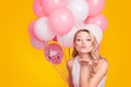 Portrait of lovely sweet chick having many air balloons blowing kiss with pout lips palm to the camera isolated on pink