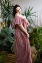 Portrait of lovely woman in pink chiffon dress, coquettishly presenting her shoulder in morning in her greenhouse.