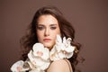 Portrait of lovely woman takes beautiful white flowers . Brunette woman with blowing hair, curly hairstyle holding orchids Royalty Free Stock Photo