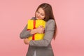 Portrait of lovely young businesswoman in suit jacket embracing gift box tightly and smiling with happiness